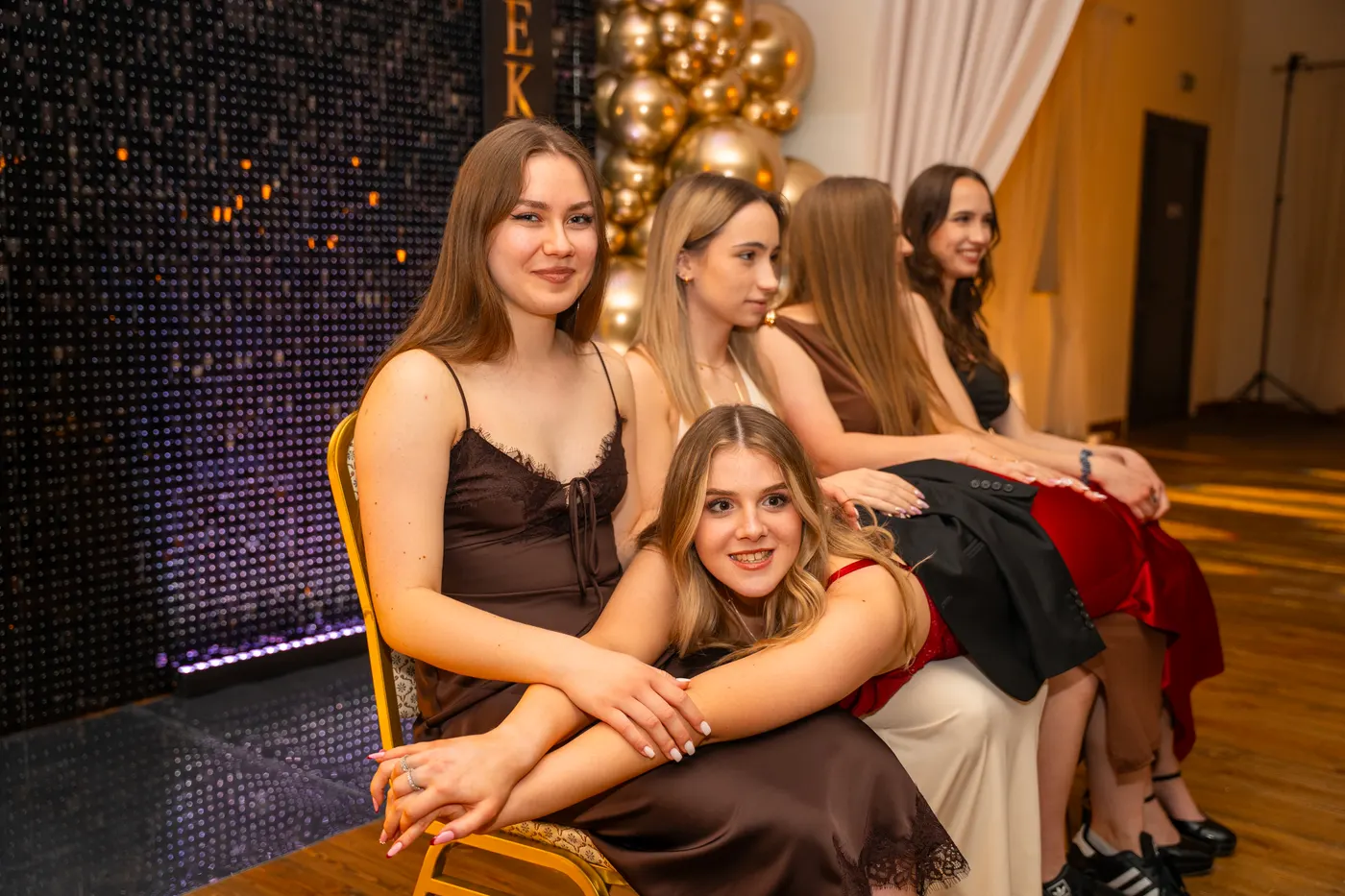Eleganckie kobiety siedzą przy złotych balonach i cekinowej ściance